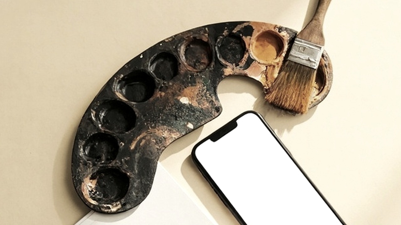 A worn paint palette and brush beside a phone showing a blank screen